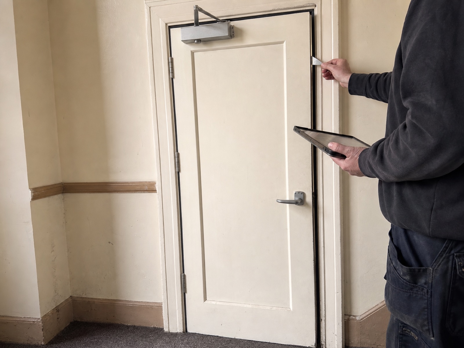 AI-generated illustrative image of a fire-door inspection in a London residential-block corridor, with door gaps and hardware being checked.