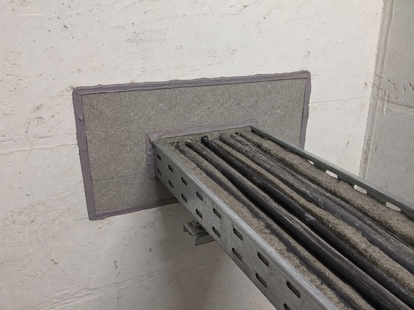 AI-generated illustrative image of completed penetration fire-stopping around building services inside a residential-block riser.