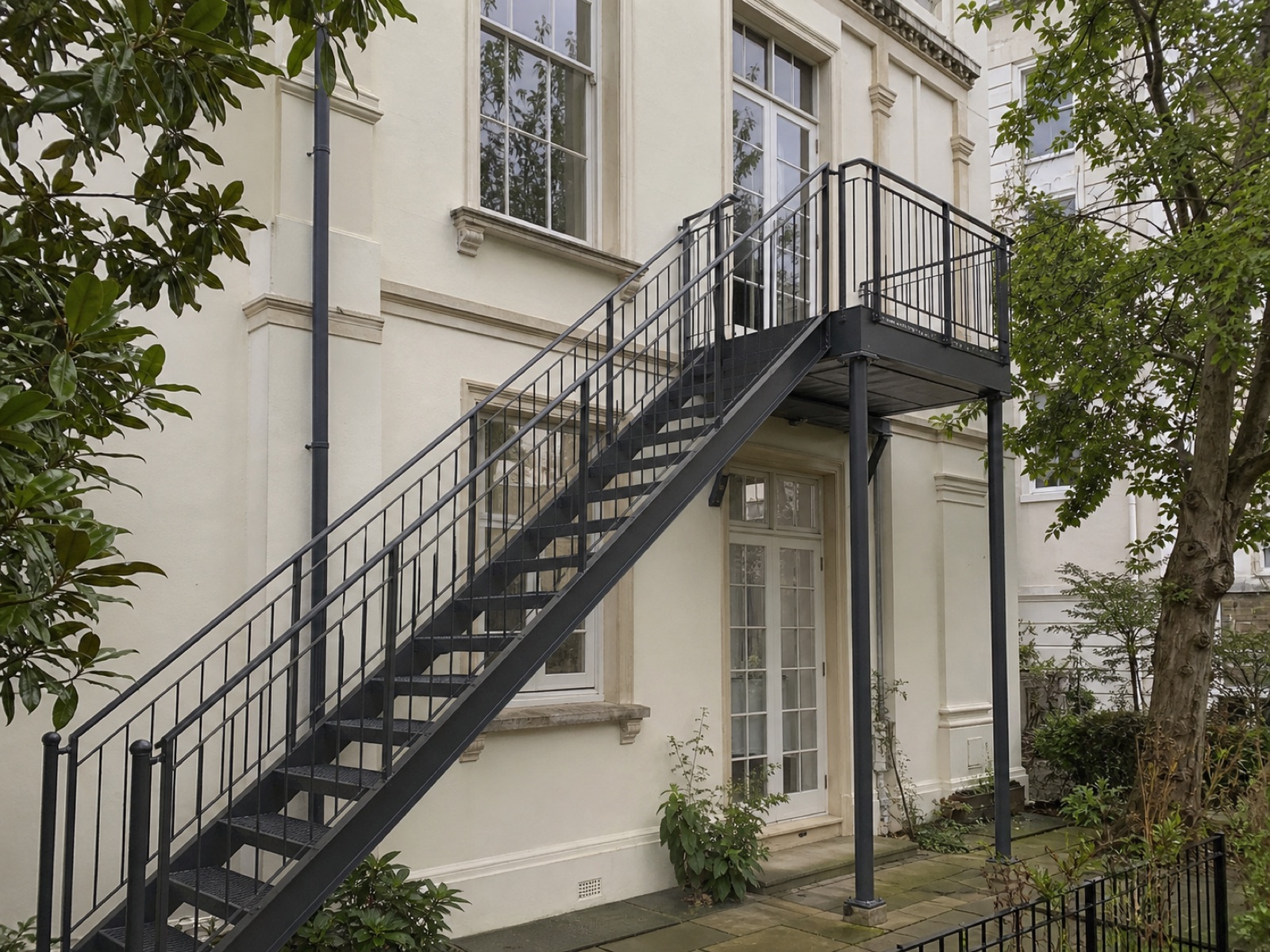 Refurbished external steel fire-escape stair and landing at a pale-stucco Belsize Park residence.