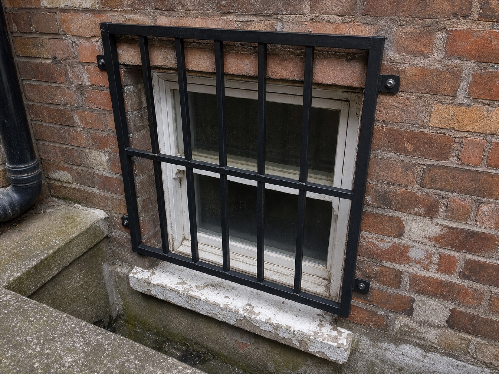 Fixed black steel security grille over a basement sash window in a London brick lightwell.
